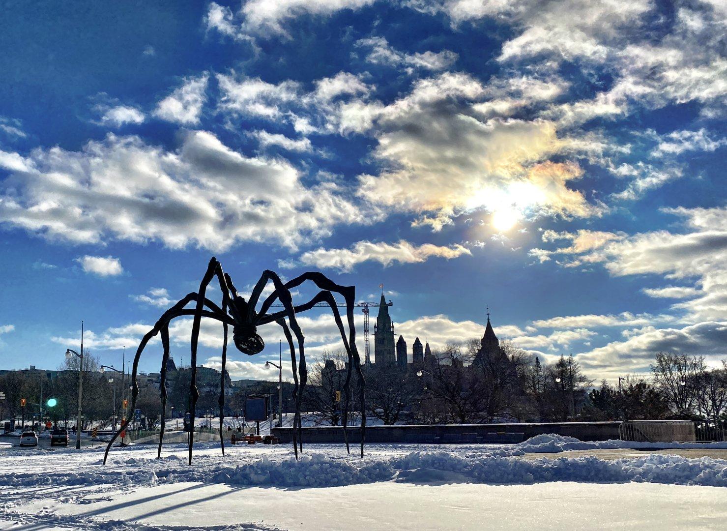 A view of Maman the spider sculpture outside of the Ottawa art gallery with the parliament buildings in the background on a very sunny day.