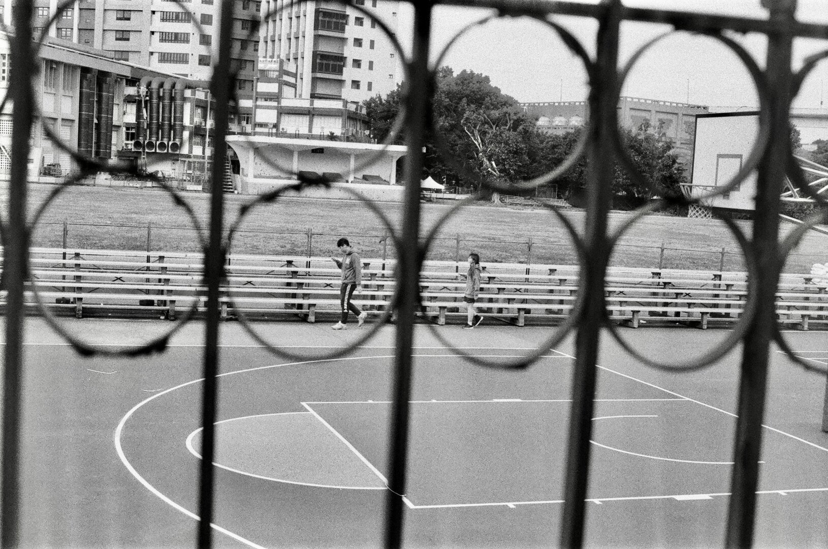 A man and a woman walking separately as seen through a fence