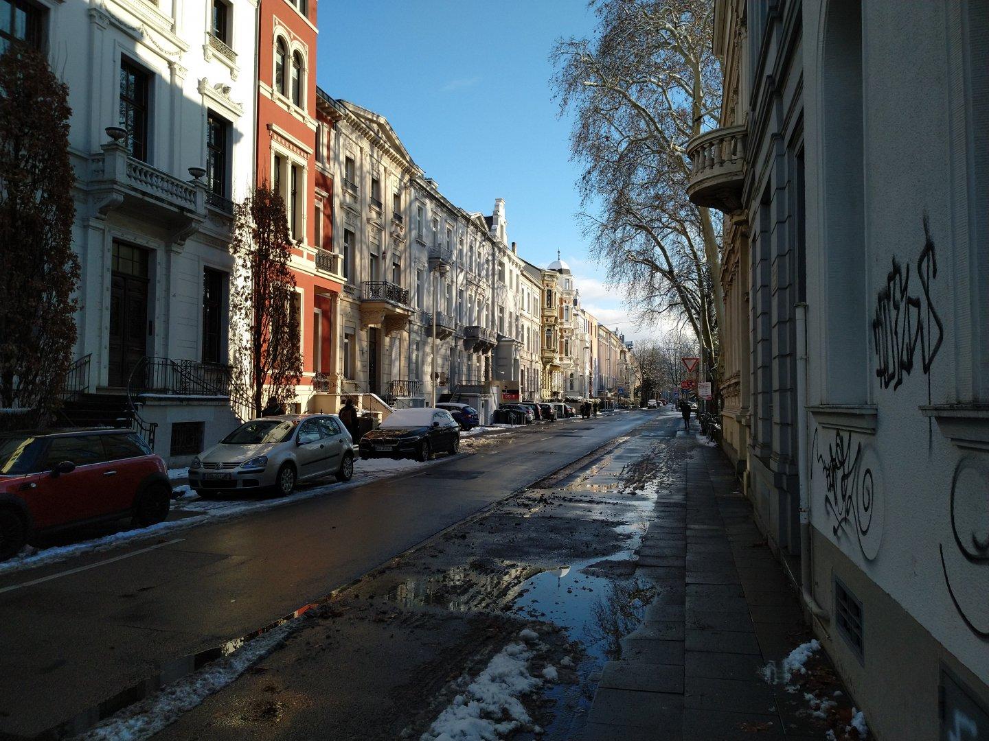 Views oft a street in Bonn, Germany. Restbof snow on the pavement on the right, house fronts glazing in the sun on the left.